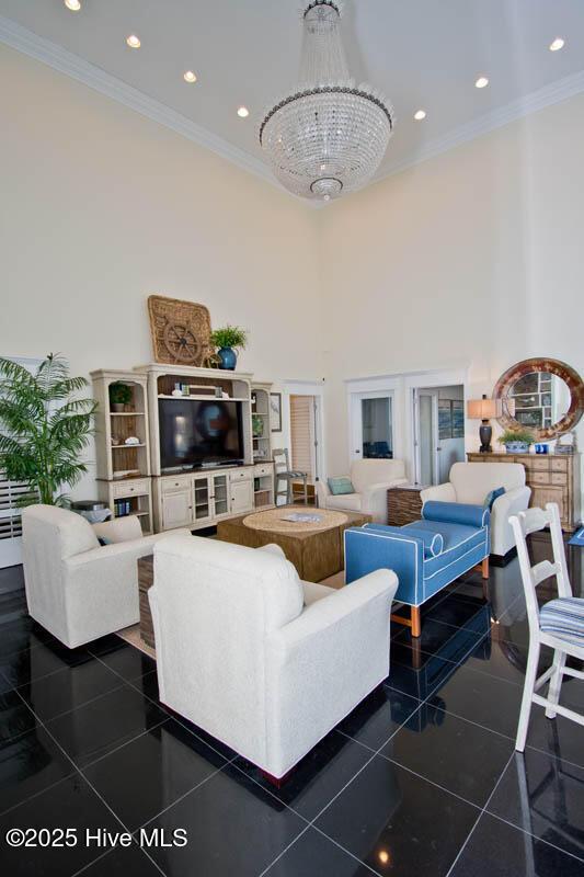 living area with ornamental molding, dark tile patterned floors, a high ceiling, and an inviting chandelier