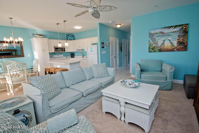 living room featuring light carpet, baseboards, and ceiling fan with notable chandelier