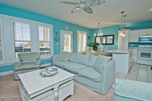 living area with light tile patterned floors, baseboards, and ceiling fan with notable chandelier