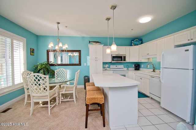 kitchen featuring white appliances, a kitchen island, white cabinetry, light countertops, and hanging light fixtures