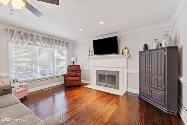 living area featuring baseboards, ornamental molding, dark wood finished floors, and a glass covered fireplace