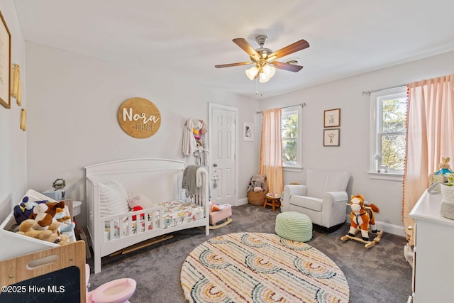 bedroom with a crib, baseboards, dark colored carpet, and a ceiling fan