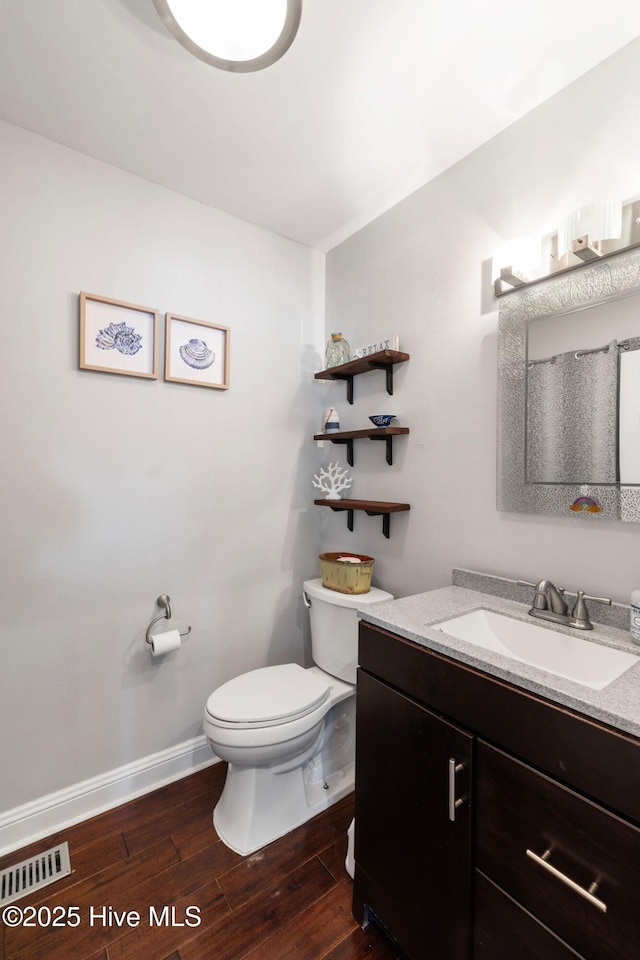 bathroom featuring toilet, wood finished floors, vanity, visible vents, and baseboards