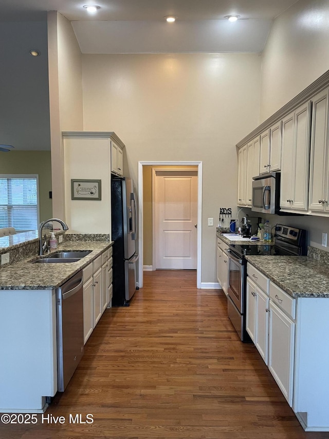 kitchen with stainless steel appliances, a towering ceiling, a sink, dark stone countertops, and wood finished floors