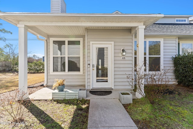 doorway to property with covered porch, a chimney, and roof with shingles