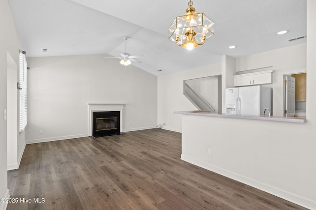 unfurnished living room with dark wood-style floors, vaulted ceiling, ceiling fan with notable chandelier, a fireplace with flush hearth, and visible vents