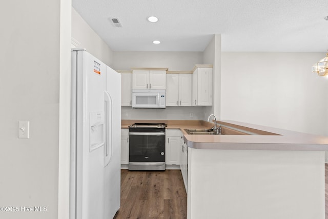 kitchen featuring a peninsula, dark wood-style floors, a sink, white appliances, and light countertops