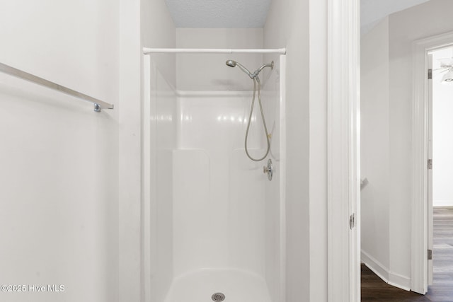 full bathroom featuring baseboards, wood finished floors, a textured ceiling, and a shower