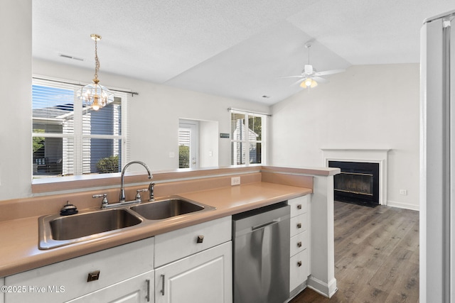 kitchen featuring vaulted ceiling, stainless steel dishwasher, a sink, white cabinetry, and ceiling fan with notable chandelier