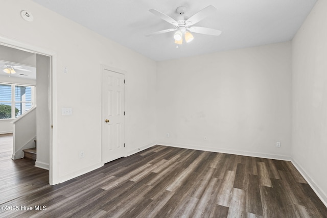 spare room with dark wood finished floors, baseboards, a ceiling fan, and stairs