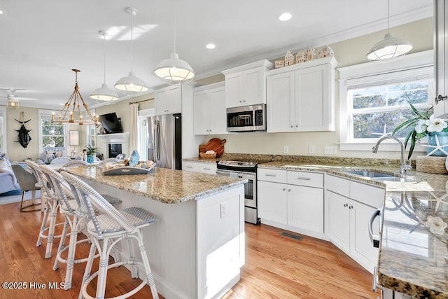 kitchen with stainless steel appliances, a center island, sink, white cabinets, and pendant lighting