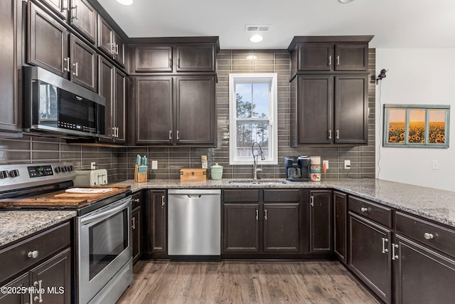 kitchen featuring visible vents, light stone counters, stainless steel appliances, dark brown cabinets, and a sink