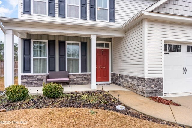 entrance to property featuring covered porch, stone siding, and an attached garage