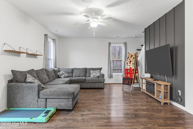 living area featuring dark wood-type flooring, baseboards, and a ceiling fan