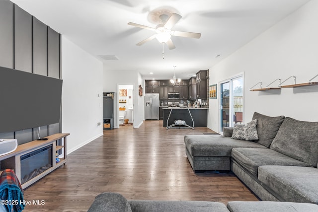 living room featuring dark wood-type flooring, baseboards, and ceiling fan with notable chandelier