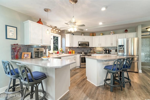 kitchen with hanging light fixtures, a kitchen breakfast bar, stainless steel appliances, white cabinets, and kitchen peninsula