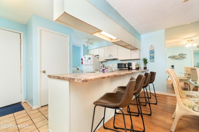 kitchen featuring kitchen peninsula, white fridge, ceiling fan, white cabinets, and a kitchen bar