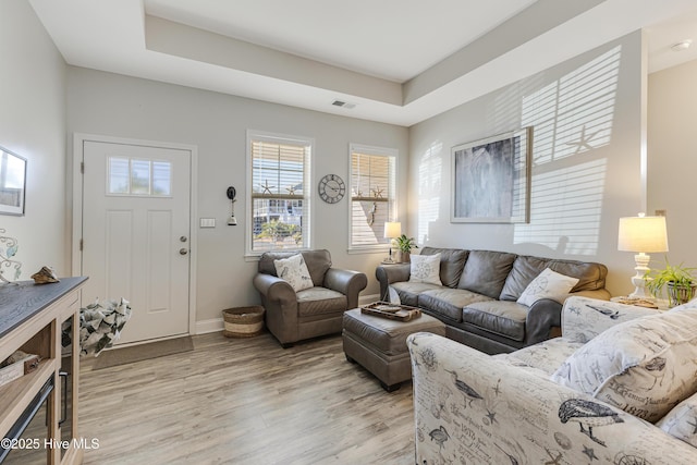 living room featuring light wood finished floors, a raised ceiling, visible vents, and baseboards