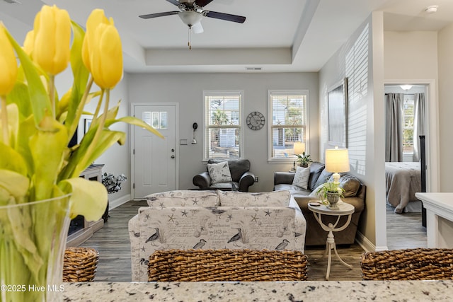 bedroom with a tray ceiling, visible vents, baseboards, and wood finished floors