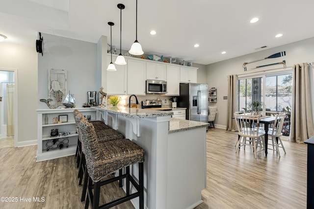 kitchen with light wood finished floors, stainless steel appliances, white cabinets, light stone countertops, and a peninsula