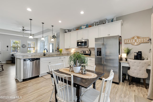 kitchen featuring a peninsula, a sink, light wood-style floors, white cabinets, and appliances with stainless steel finishes