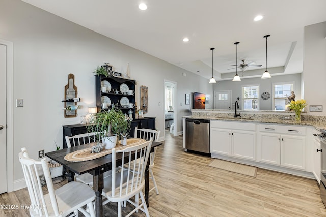 kitchen featuring dishwasher, a tray ceiling, light wood-type flooring, white cabinetry, and a sink