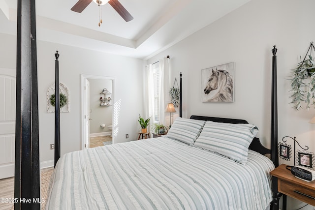 bedroom with a raised ceiling, connected bathroom, baseboards, and ceiling fan