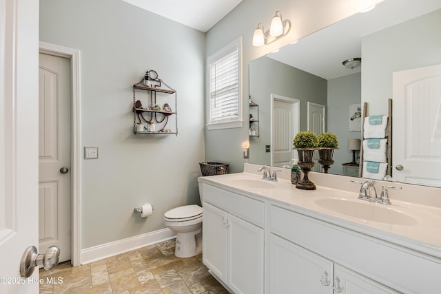 bathroom featuring double vanity, baseboards, toilet, and a sink