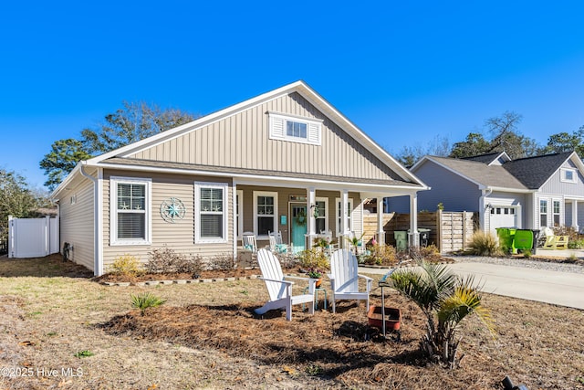 view of front of home featuring board and batten siding, covered porch, fence, and concrete driveway