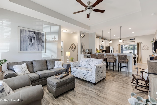 living room featuring a ceiling fan, light wood-type flooring, a raised ceiling, and recessed lighting