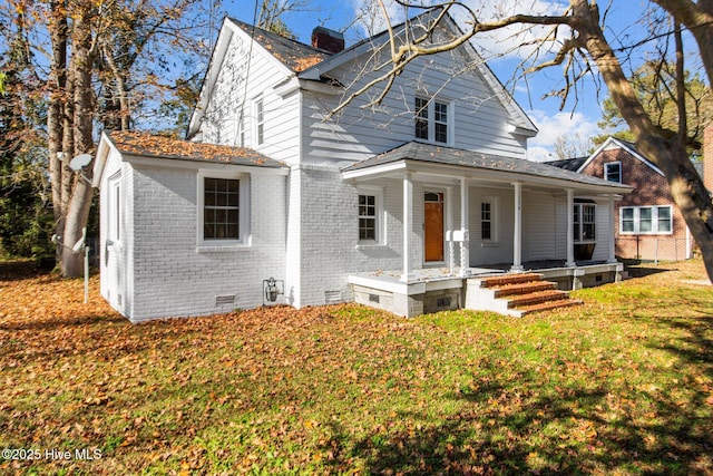 view of front of house featuring brick siding, a front lawn, a porch, a chimney, and crawl space