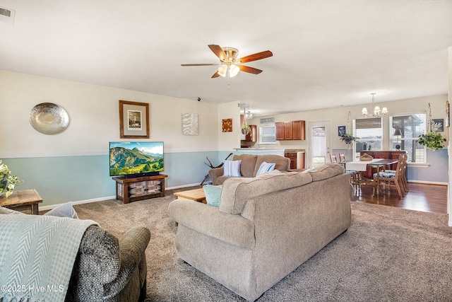 living area featuring ceiling fan with notable chandelier, carpet, visible vents, and baseboards