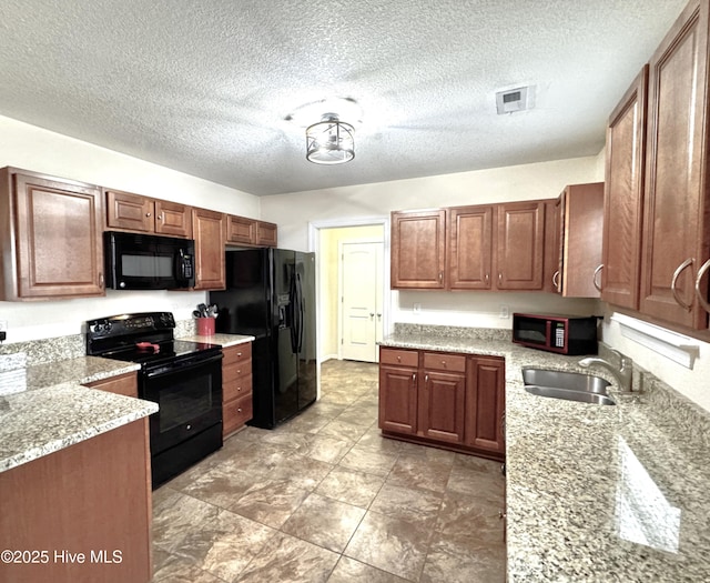 kitchen featuring visible vents, brown cabinetry, a sink, light stone countertops, and black appliances