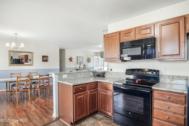 kitchen with black appliances, a peninsula, light stone countertops, and brown cabinets