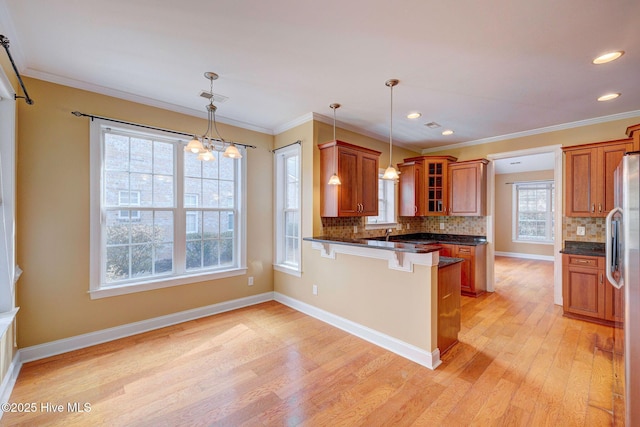 kitchen featuring brown cabinetry, light wood-style floors, glass insert cabinets, a peninsula, and a kitchen bar