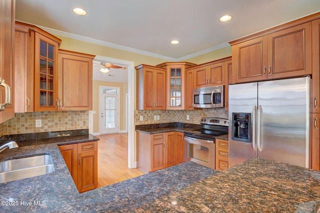 kitchen with appliances with stainless steel finishes, dark stone countertops, crown molding, light wood-style floors, and a sink