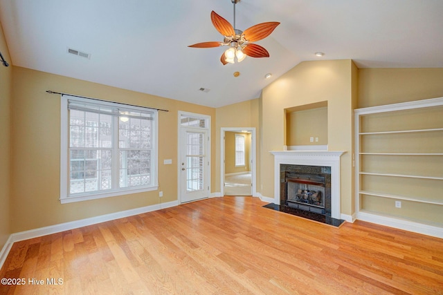 unfurnished living room featuring lofted ceiling, visible vents, a high end fireplace, wood finished floors, and baseboards