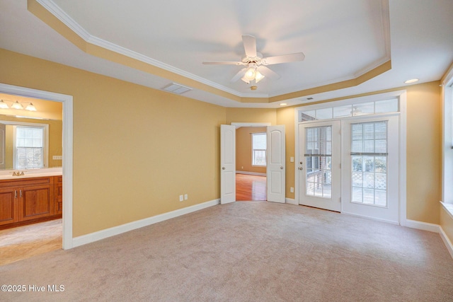 empty room with light carpet, a tray ceiling, ornamental molding, and baseboards