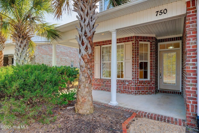 view of exterior entry featuring a porch and brick siding