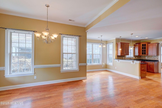 kitchen with brown cabinetry, dark countertops, a kitchen breakfast bar, light wood-style floors, and a notable chandelier