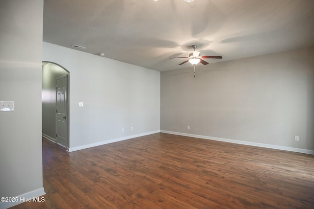 empty room featuring dark wood-style flooring, ceiling fan, baseboards, arched walkways, and visible vents