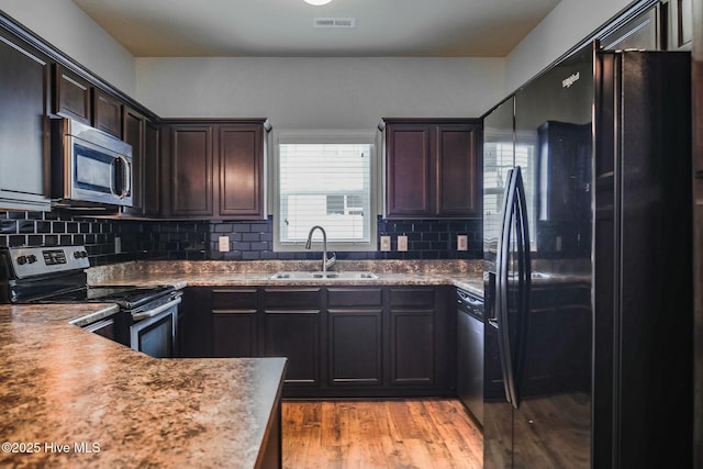 kitchen featuring dark brown cabinets, backsplash, stainless steel appliances, light wood-style flooring, and a sink