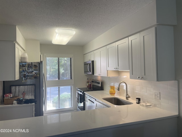 kitchen with light countertops, backsplash, appliances with stainless steel finishes, white cabinets, and a sink