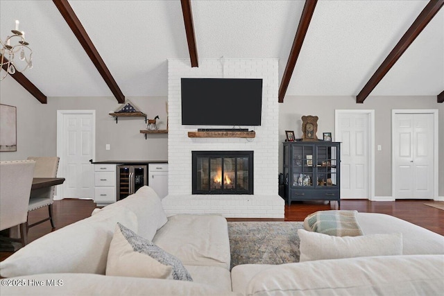 living room featuring wine cooler, dark wood-style flooring, vaulted ceiling with beams, a brick fireplace, and a textured ceiling