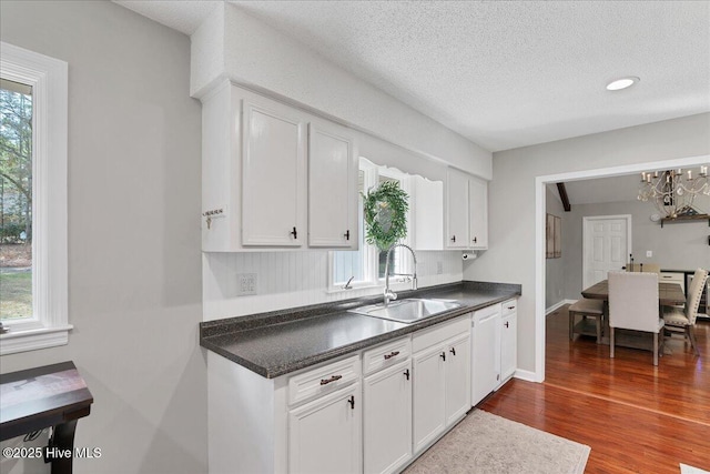 kitchen with dark wood-type flooring, dark countertops, a sink, and white cabinetry