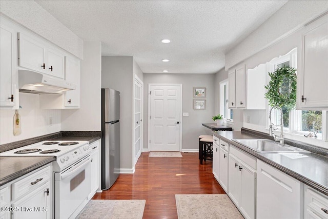 kitchen featuring dark countertops, white appliances, a sink, and under cabinet range hood