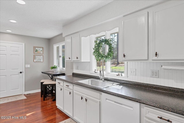 kitchen with dishwasher, dark countertops, a sink, and white cabinets