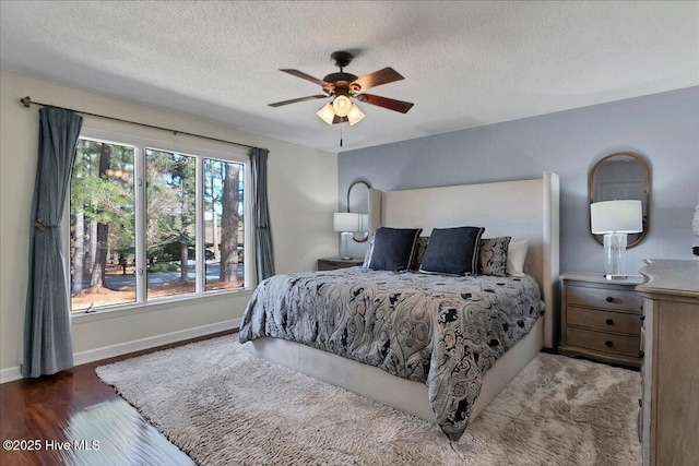 bedroom featuring ceiling fan, a textured ceiling, baseboards, and wood finished floors