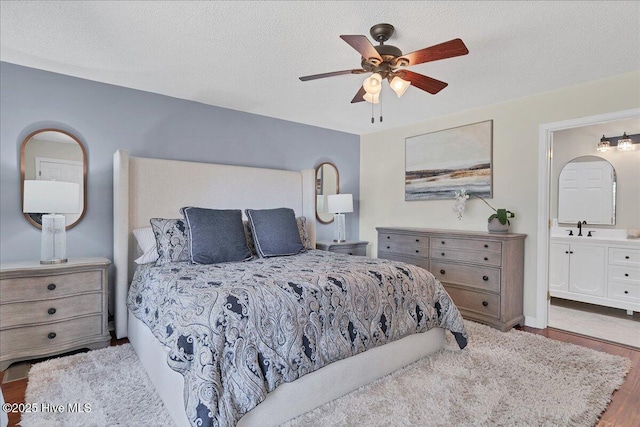 bedroom featuring ceiling fan, ensuite bath, light wood-style flooring, a textured ceiling, and a sink