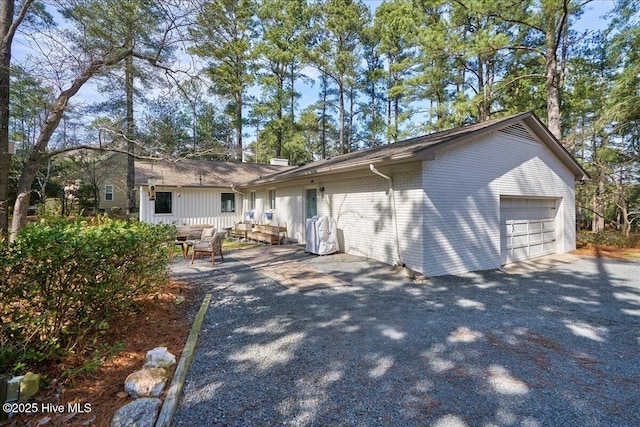 view of front of home featuring aphalt driveway, brick siding, a chimney, an attached garage, and a patio area